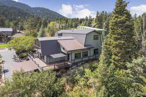 Back of property with a gambrel roof, a forest view, a deck with mountain view, and a metal roof