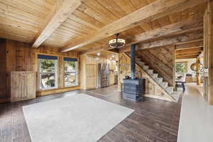 Unfurnished living room with wooden walls, a wood stove, healthy amount of natural light, stairway, and a wood ceiling with exposed beams