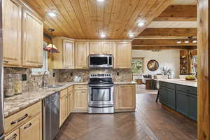 Kitchen with stainless steel appliances, tasteful backsplash, decorative light fixtures, light stone countertops, and light brown cabinets
