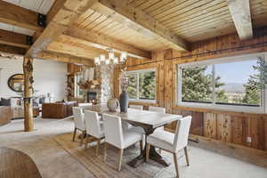 Dining area with wood walls, a fireplace, a wood ceiling with exposed beams, and a chandelier