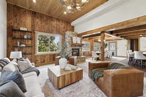 Living room featuring wood walls, a chandelier, wooden ceiling, a stone fireplace, and recessed lighting