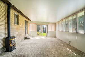 Unfurnished sunroom with carpet, brick wall, vaulted ceiling, and a wood stove