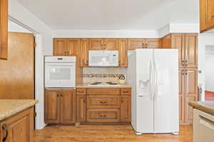 Kitchen with white appliances, decorative backsplash, light wood-style floors, and brown cabinetry