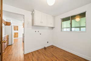 Laundry area with light wood-style floors, cabinet space, electric dryer hookup, and washer hookup