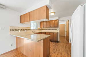 Kitchen featuring freestanding refrigerator, a peninsula, dark wood-style floors, light stone countertops, and brown cabinets