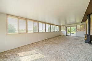 Unfurnished sunroom featuring a wood stove, carpet floors, and vaulted ceiling