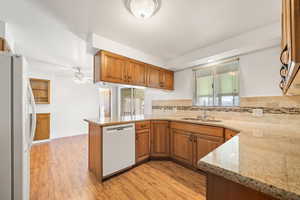Kitchen featuring brown cabinets, white appliances, light wood-style floors, light stone countertops, and a ceiling fan