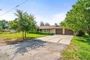 View of front of home featuring driveway, an attached garage, a front yard, a chimney, and brick siding