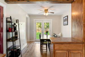 Dining space with light wood finished floors, a ceiling fan, a textured ceiling, and french doors