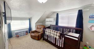 Bedroom featuring a textured ceiling, vaulted ceiling, a nursery area, light carpet, and a wall mounted AC