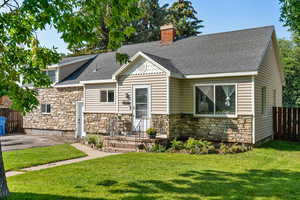 View of front facade with stone siding, roof with shingles, and a chimney