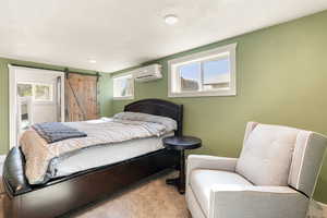 Bedroom with carpet flooring, a barn door, multiple windows, an AC wall unit, and a textured ceiling