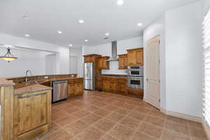Kitchen with brown cabinets, stainless steel appliances, recessed lighting, wall chimney exhaust hood, and dark stone counters