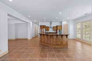 Kitchen with a kitchen breakfast bar, brown cabinets, recessed lighting, a large island, and light tile patterned flooring