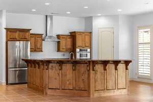 Kitchen featuring a breakfast bar, brown cabinetry, stainless steel appliances, light tile patterned floors, and recessed lighting