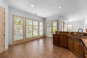 Kitchen with healthy amount of natural light, light tile patterned flooring, recessed lighting, dark stone countertops, and dark brown cabinetry
