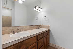 Bathroom with double vanity, backsplash, and dark tile patterned flooring