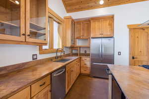 Kitchen featuring stainless steel appliances, glass insert cabinets, wood ceiling, dark stone countertops, and light brown cabinets