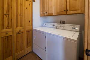 Laundry room featuring washing machine and clothes dryer, cabinet space, and dark tile patterned flooring