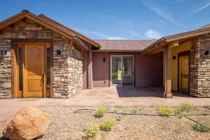 Entrance to property featuring stone siding, stucco siding, a metal roof, and a patio area