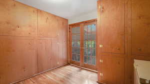Storage room featuring french doors, light hardwood / wood-style flooring, and wooden cabinets