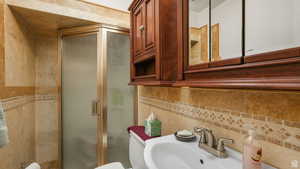 Half bathroom ensuite featuring sink, a shower with shower door, toilet, tile walls, and decorative backsplash