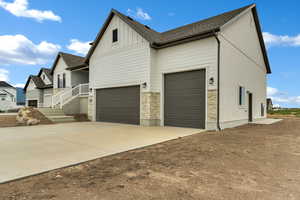 View of side of property featuring board and batten siding, a garage, stone siding, concrete driveway, and a shingled roof