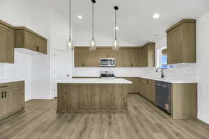 Kitchen featuring decorative light fixtures, tasteful backsplash, vaulted ceiling, a center island, and appliances with stainless steel finishes