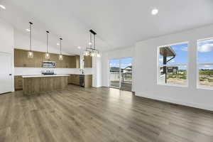 Kitchen with pendant lighting, light countertops, open floor plan, decorative backsplash, and vaulted ceiling