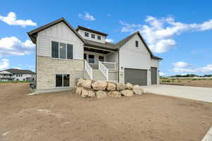 View of front of property with stone siding, board and batten siding, stairs, a porch, and concrete driveway