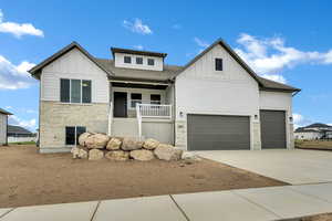 Modern farmhouse featuring stone siding, board and batten siding, a porch, and a shingled roof