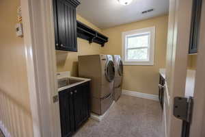 Washroom with cabinet space, washer and dryer, and light colored carpet