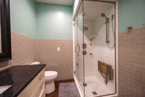 Full bathroom with tile walls, vanity, a stall shower, and a wainscoted wall