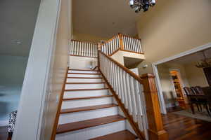 Stairway with a chandelier, wood finished floors, and a high ceiling