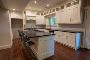 Kitchen featuring a kitchen bar, white cabinetry, glass insert cabinets, dark stone countertops, and recessed lighting