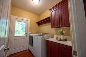Laundry room featuring a textured ceiling, dark wood-style floors, washer and clothes dryer, and cabinet space