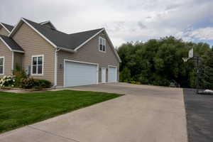 View of side of home with driveway, a shingled roof, an attached garage, and a yard