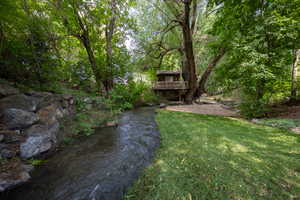 View of green lawn featuring a deck with water view and a forest view