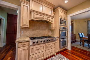 Kitchen featuring cream cabinets, appliances with stainless steel finishes, dark wood-type flooring, light stone countertops, and recessed lighting