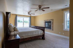 Carpeted bedroom with a textured ceiling, a ceiling fan, and a stone fireplace