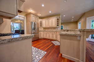 Kitchen with stainless steel fridge with ice dispenser, a peninsula, dark wood-style floors, a chandelier, and recessed lighting