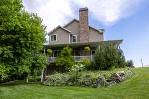 Back of property with a yard, a porch, stone siding, and a chimney