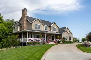 View of front of property with a front yard, covered porch, a chimney, concrete driveway, and a shingled roof