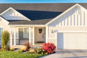 Entrance to property with board and batten siding, covered porch, a shingled roof, an attached garage, and driveway
