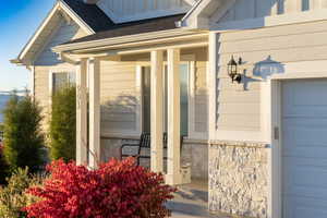 Doorway to property with a porch, stone siding, a shingled roof, and a garage