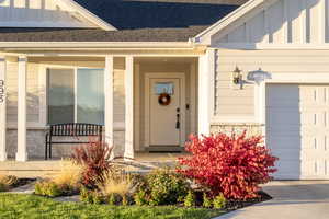 View of exterior entry featuring board and batten siding, a shingled roof, stone siding, a porch, and an attached garage