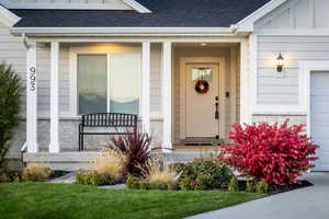 View of exterior entry featuring a shingled roof, stone siding, a garage, and a porch