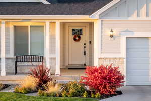 Entrance to property featuring roof with shingles, stone siding, board and batten siding, and a garage