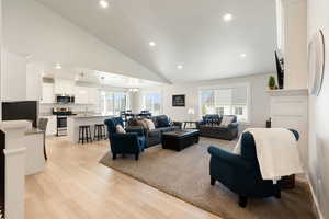 Living area with recessed lighting, healthy amount of natural light, light wood-style flooring, a chandelier, and high vaulted ceiling