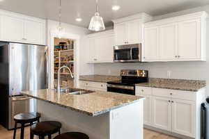 Kitchen featuring appliances with stainless steel finishes, light stone countertops, an island with sink, white cabinetry, and a kitchen breakfast bar